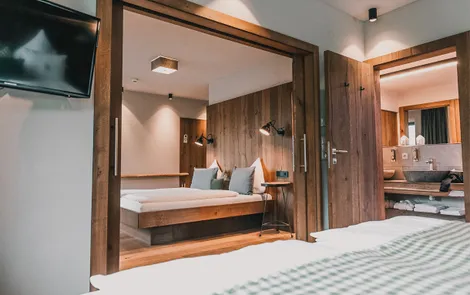 "Der Salzburger" & "Hohen Salzburg" Modernes Hotelzimmer mit Holzeinrichtung, Doppelbett und offenem Blick ins Bad